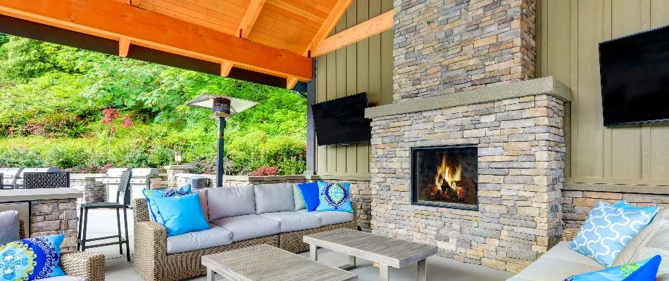 An outdoor fireplace in Huntsville, AL, with tables, chairs, and mounted televisions.