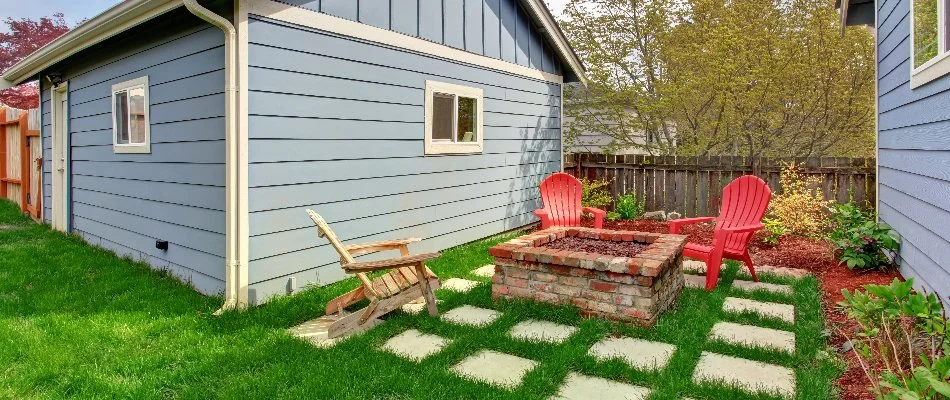 A brick, square fire pit in Huntsville, AL, with red chairs and a blue shed.